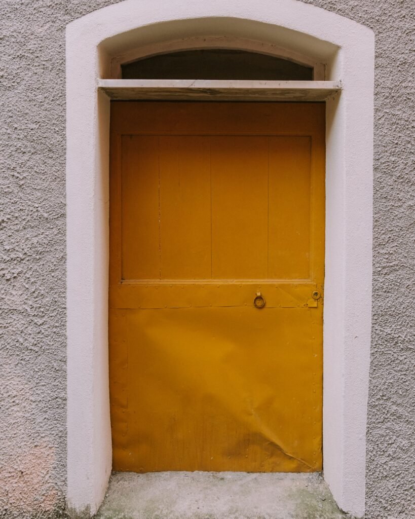 Close-up of a rustic yellow door set in a textured wall, featuring an arched frame.